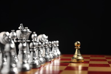 Photo of Golden pawn in front of silver chess pieces on chessboard against black background, closeup. Competition concept