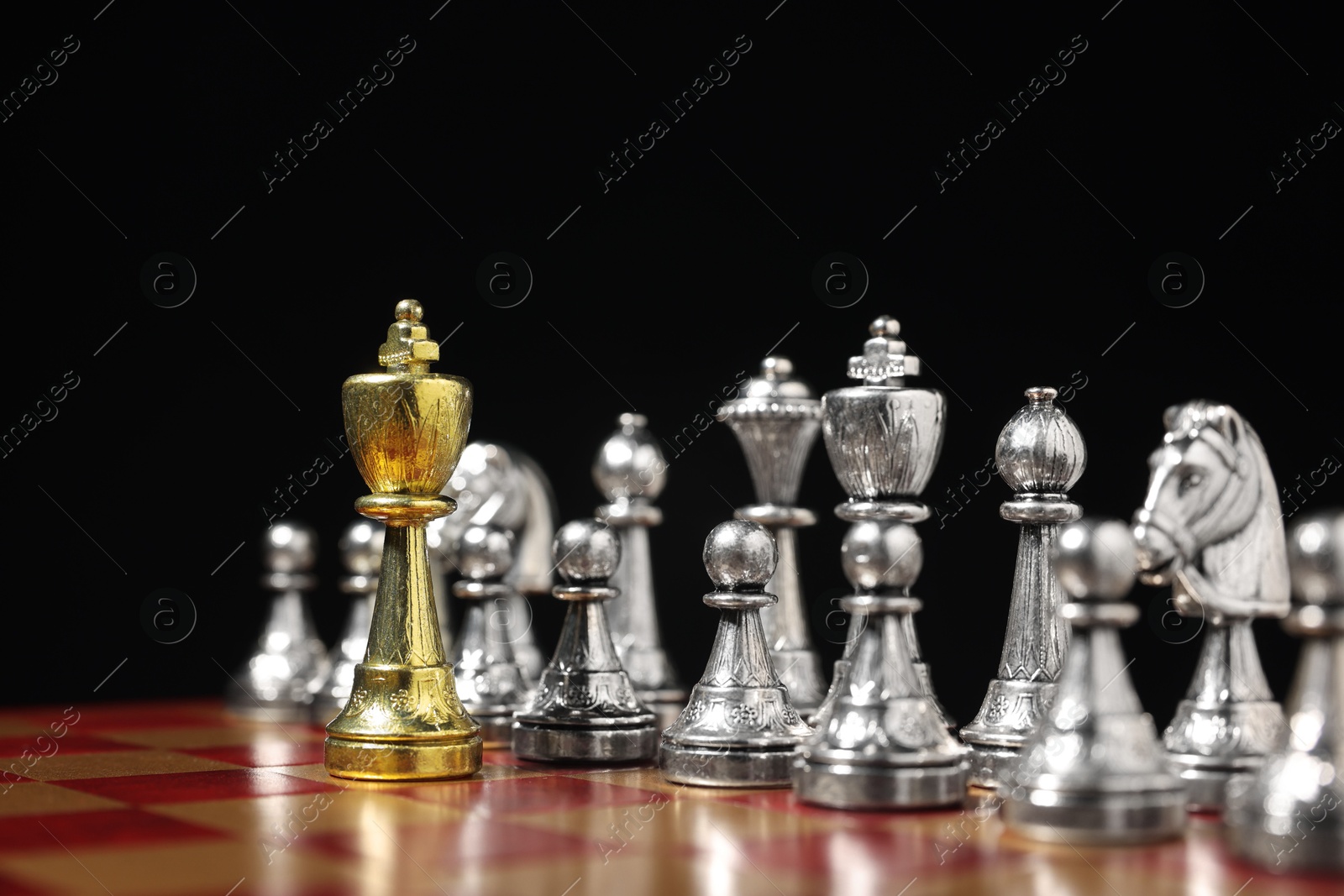 Photo of Golden king in front of silver chess pieces on chessboard against black background, closeup. Competition concept