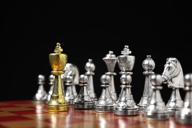 Photo of Golden king in front of silver chess pieces on chessboard against black background, closeup. Competition concept