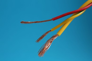 Photo of Stripped electrical wires with copper strands on light blue background, closeup