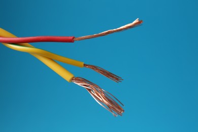 Photo of Stripped electrical wires with copper strands on light blue background, closeup