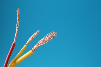 Photo of Stripped electrical wires with copper strands on light blue background, closeup. Space for text