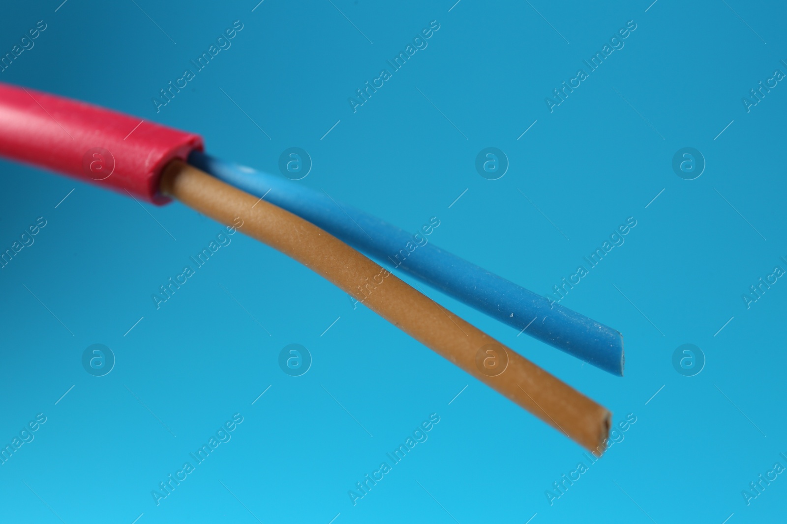 Photo of Red stripped electrical wire on light blue background, closeup