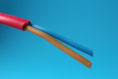 Photo of Red stripped electrical wire on light blue background, closeup