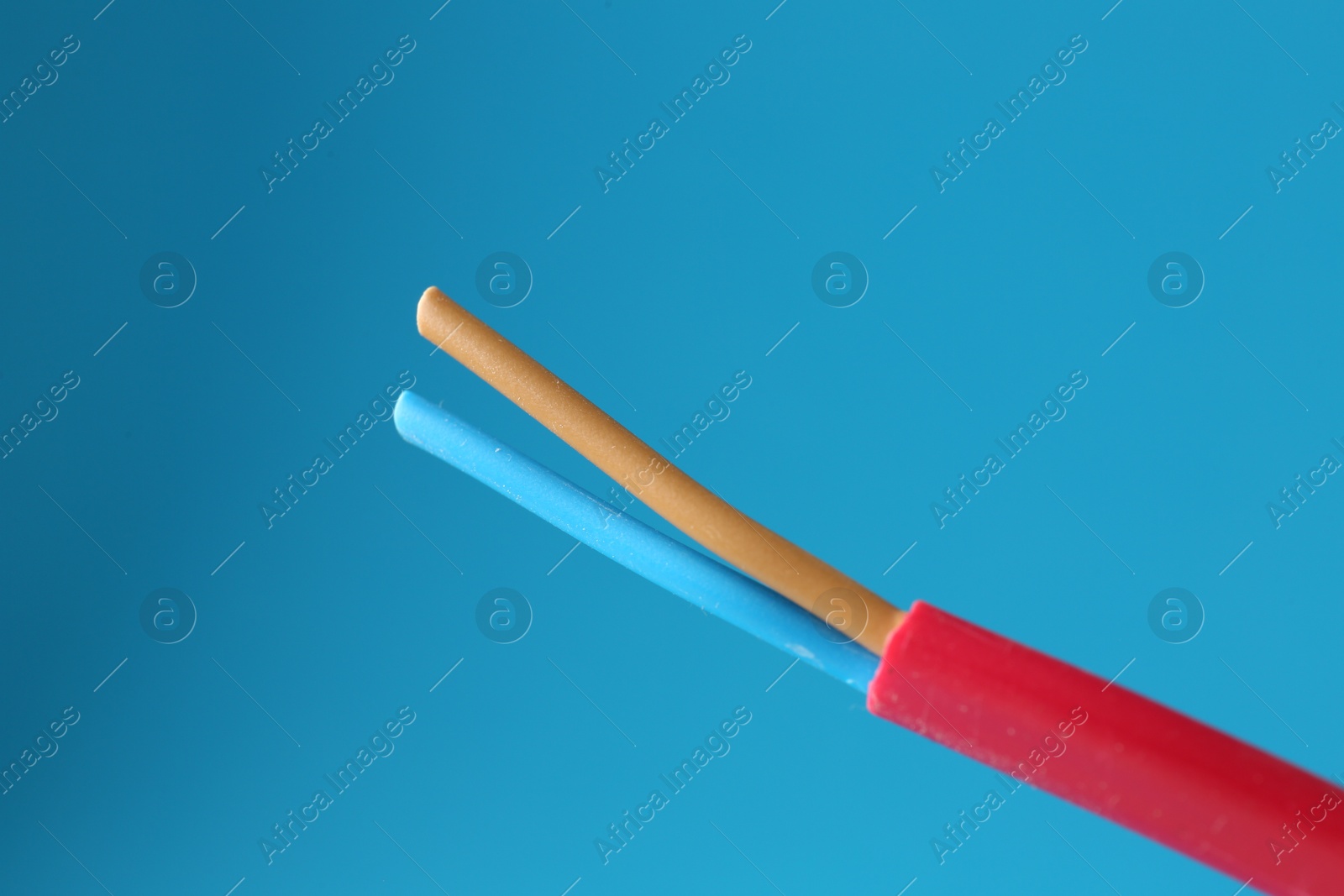 Photo of Red stripped electrical wire on light blue background, closeup