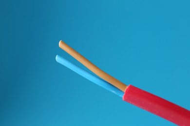 Photo of Red stripped electrical wire on light blue background, closeup