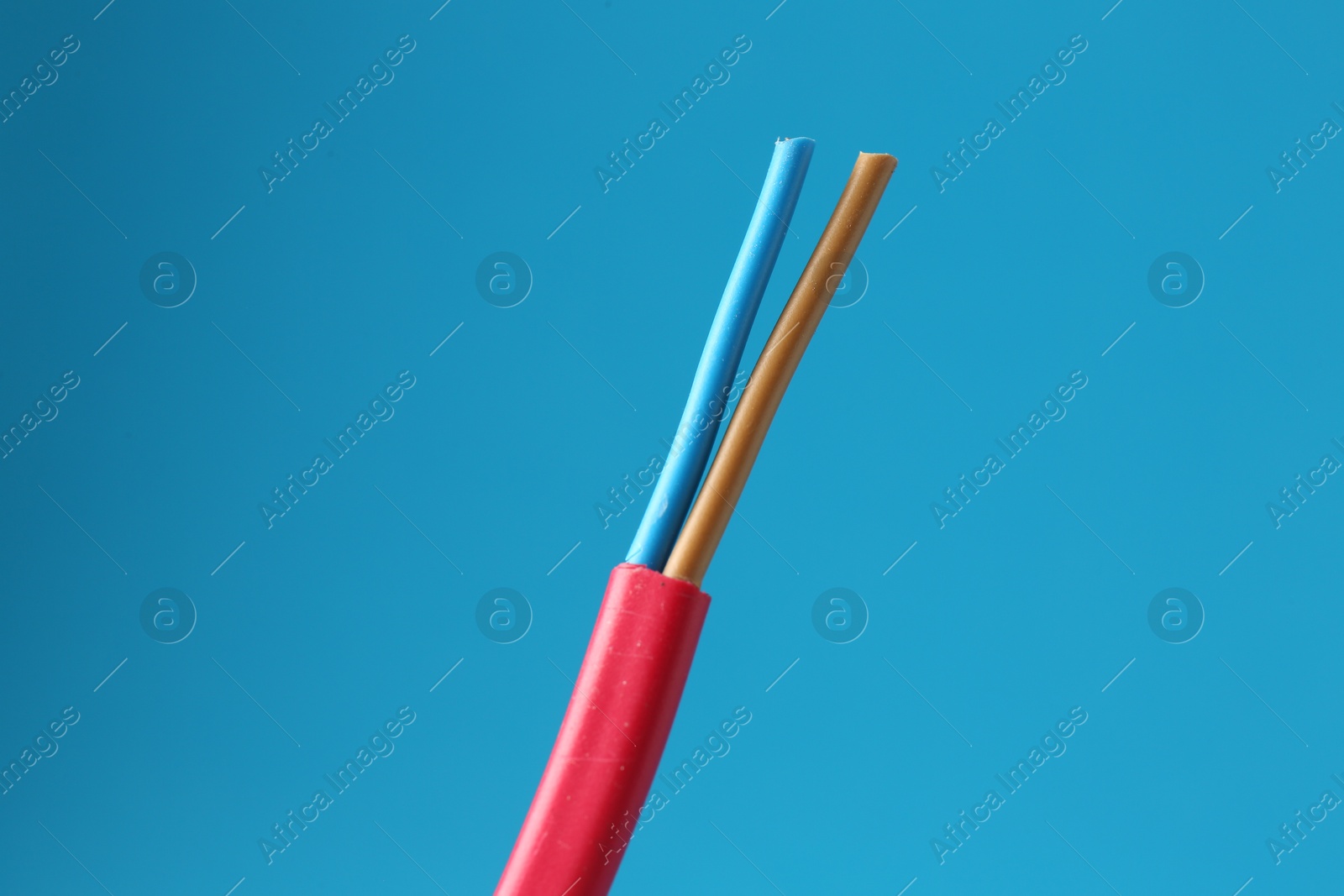 Photo of Red stripped electrical wire on light blue background, closeup