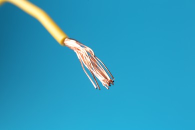 Photo of Stripped electrical wire with copper strands on light blue background, closeup