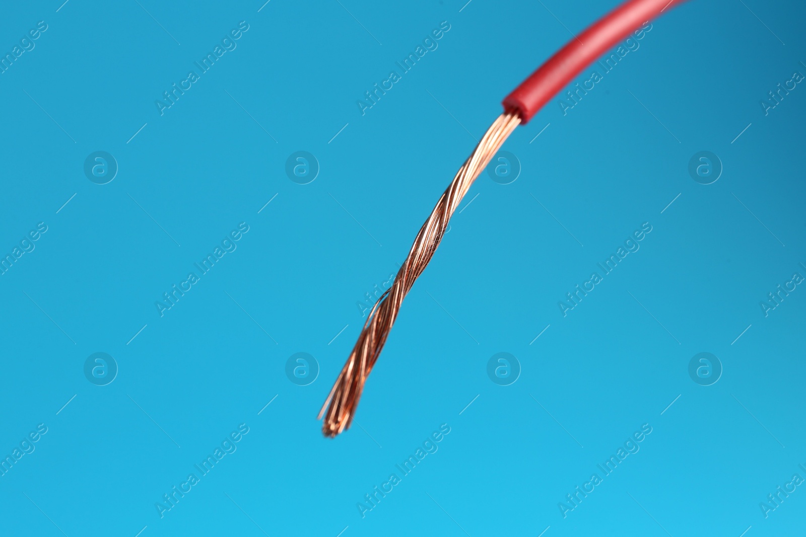 Photo of Stripped electrical wire with copper strands on light blue background, closeup