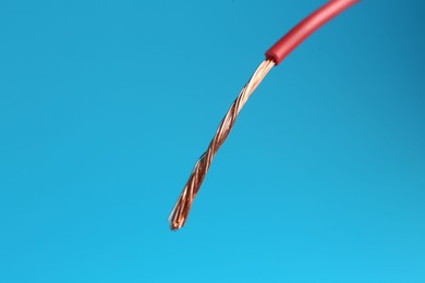 Photo of Stripped electrical wire with copper strands on light blue background, closeup