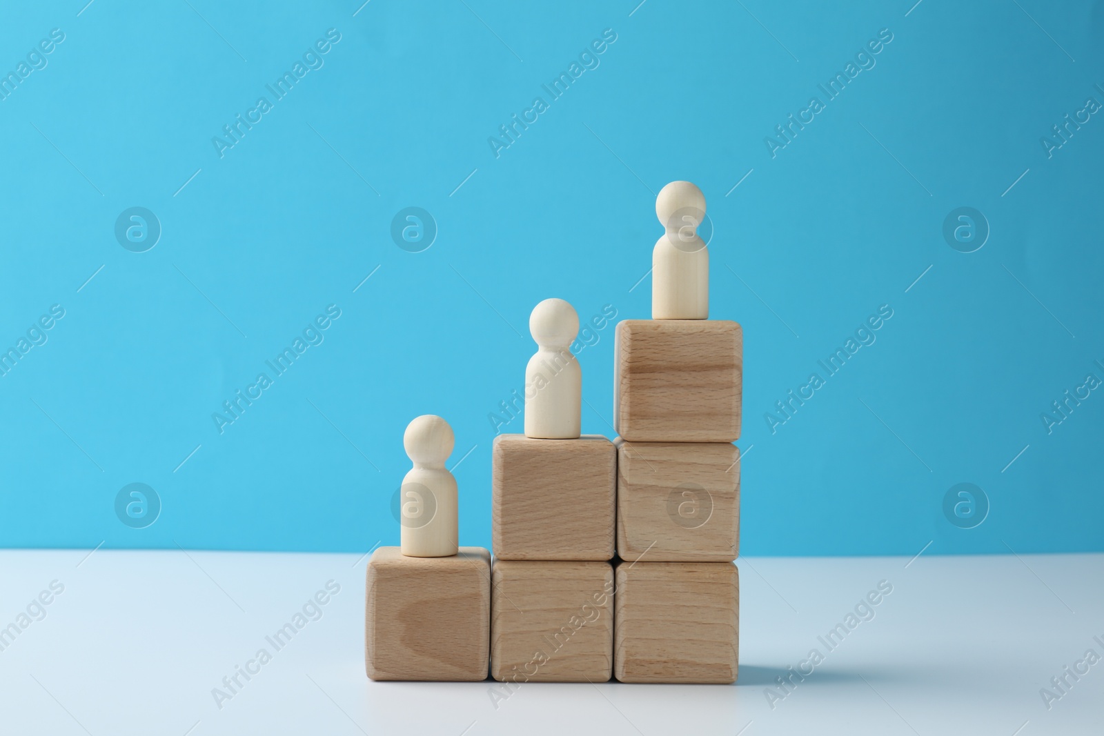 Photo of Human figures on stacked wooden blocks on white table against light blue background. Competition concept