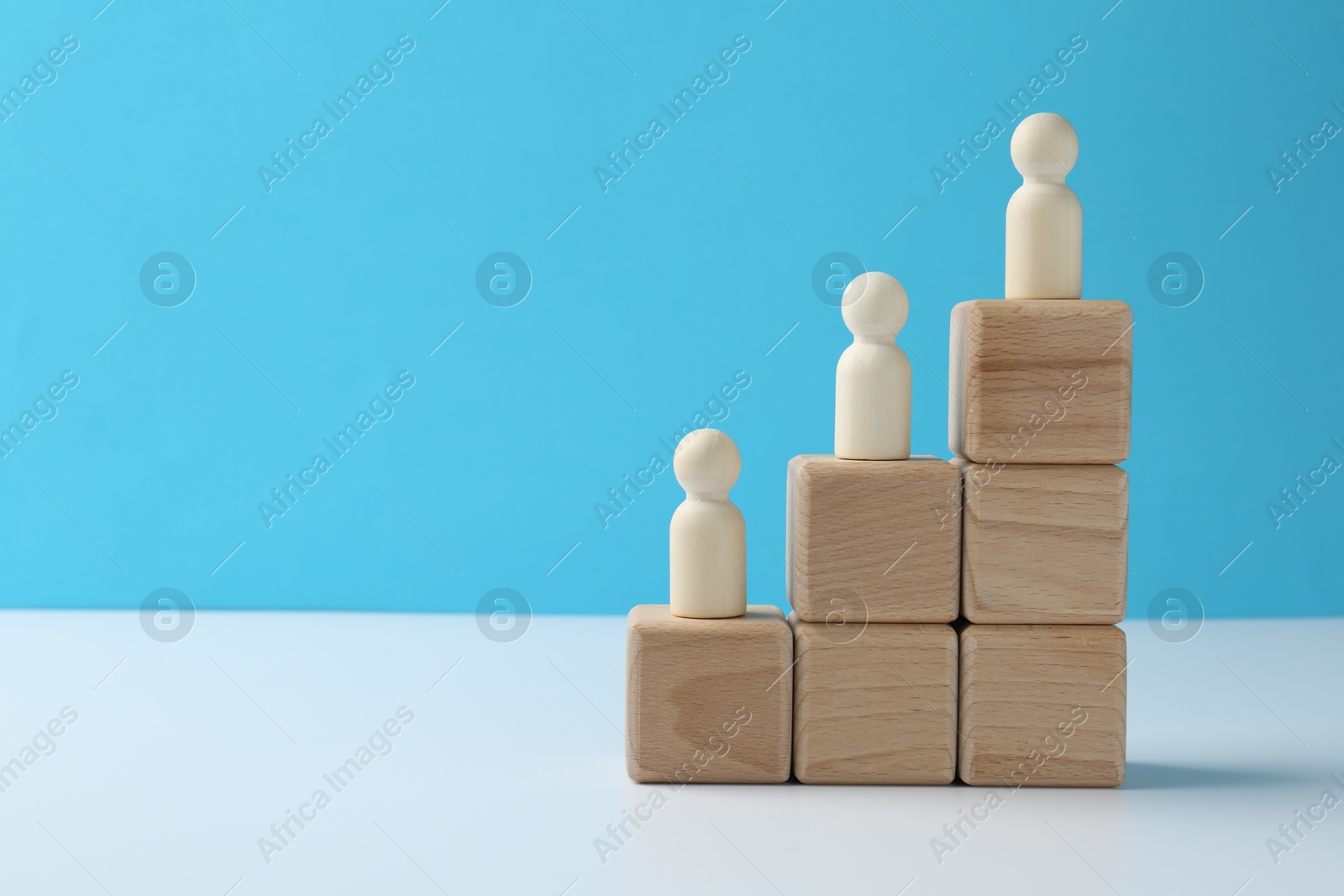 Photo of Human figures on stacked wooden blocks on white table against light blue background. Competition concept