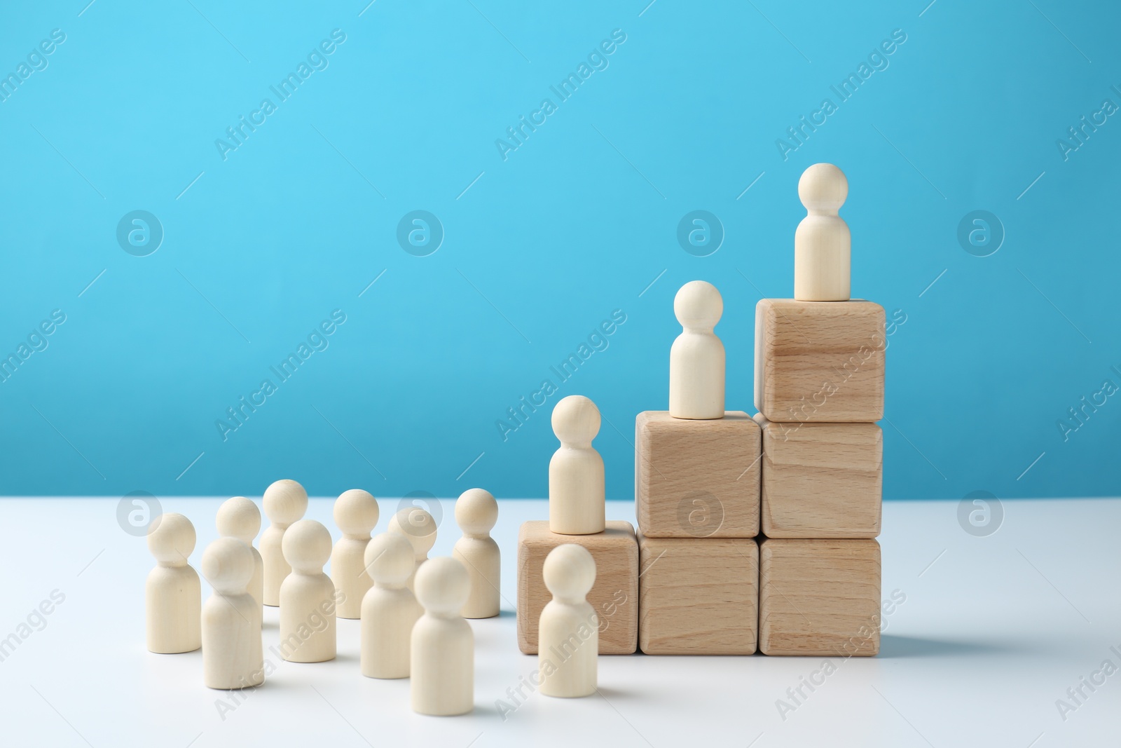 Photo of Human figures on stacked wooden blocks on white table against light blue background. Competition concept