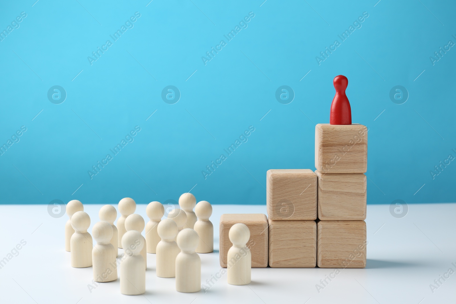 Photo of Human figures in front of stacked wooden blocks with red figure on top against light blue background. Competition concept