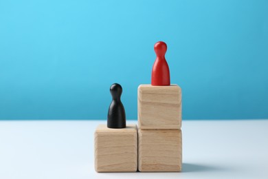 Photo of Human figures on stacked wooden blocks, red one on top against light blue background. Competition concept