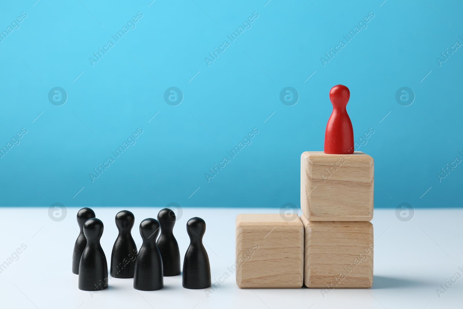 Photo of Black human figures in front of stacked wooden blocks with red figure on top against light blue background. Competition concept