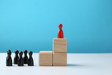 Photo of Black human figures in front of stacked wooden blocks with red figure on top against light blue background. Competition concept