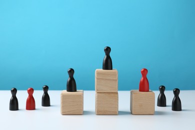 Photo of Human figures, black one on top of stacked wooden blocks on white table against light blue background. Competition concept