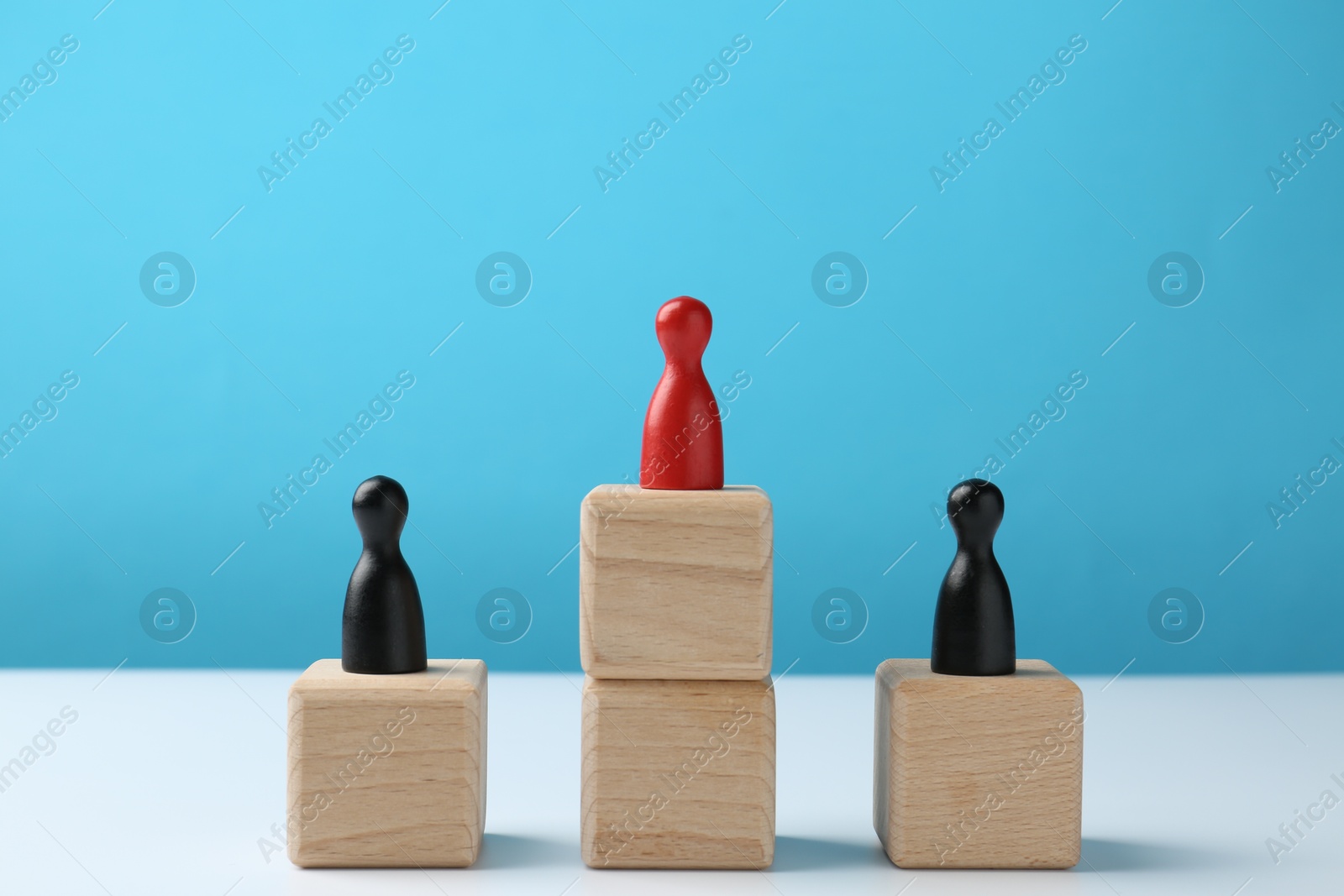 Photo of Human figures on wooden blocks, red one on top against light blue background. Competition concept