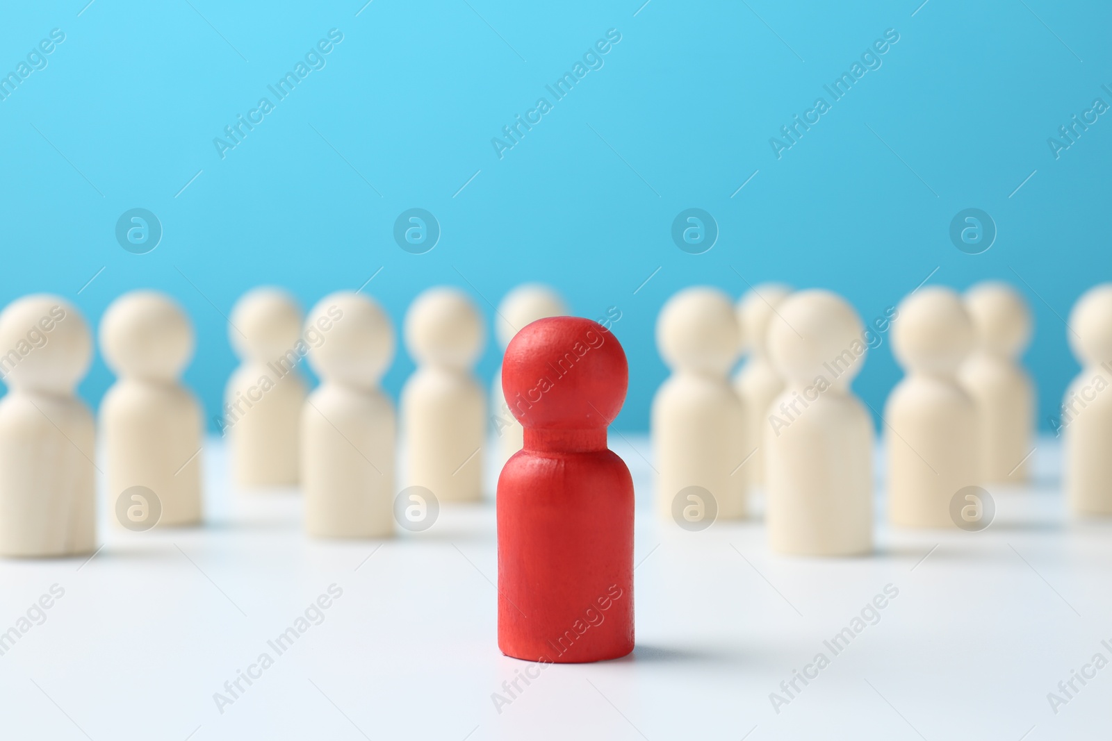 Photo of Red figure among white ones on table against light blue background. Competition concept