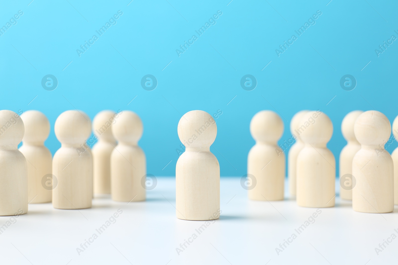 Photo of One human figure standing out among others on white table against light blue background. Competition concept