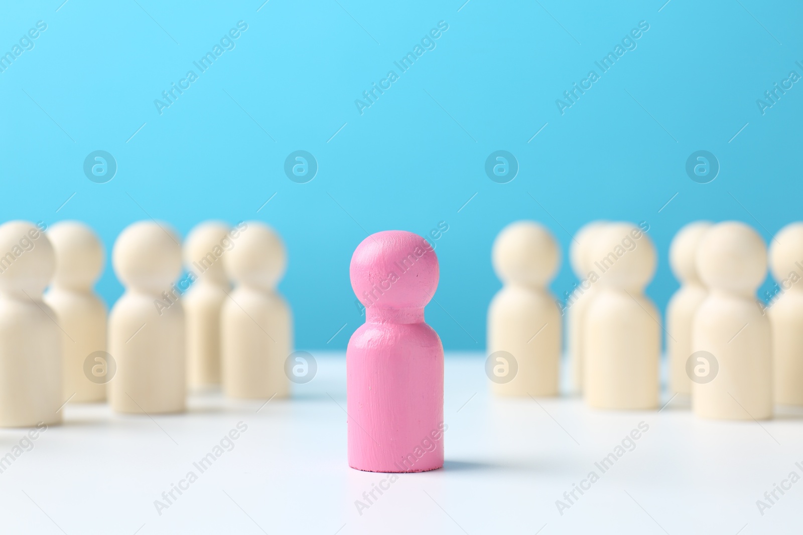 Photo of Pink figure among white ones on table against light blue background. Competition concept