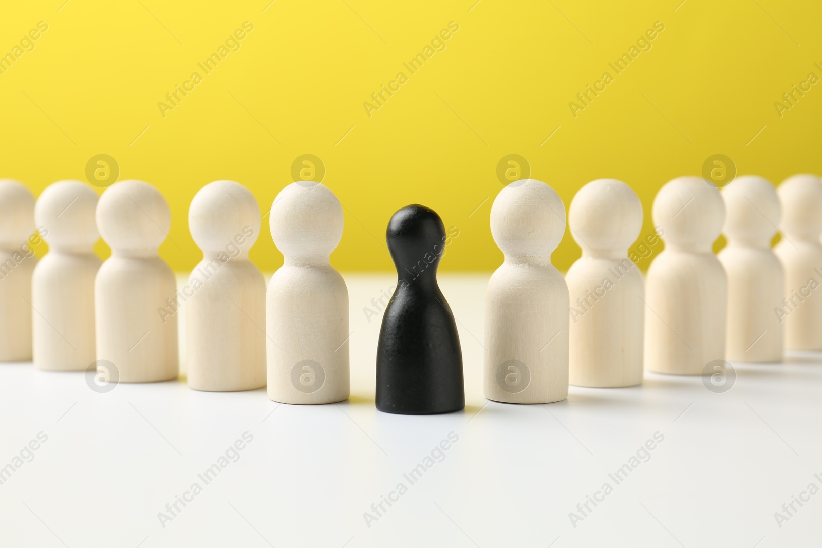 Photo of Black figure among white ones on table against yellow background. Competition concept