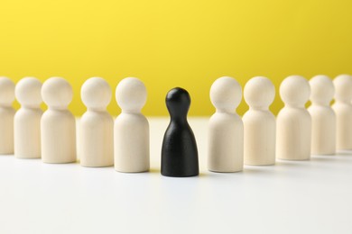 Photo of Black figure among white ones on table against yellow background. Competition concept