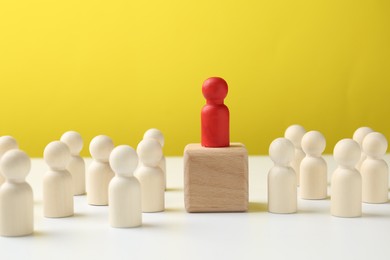 Photo of Human figures around wooden block with red figure on top against yellow background. Competition concept