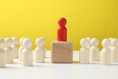 Photo of Human figures around wooden block with red figure on top against yellow background. Competition concept