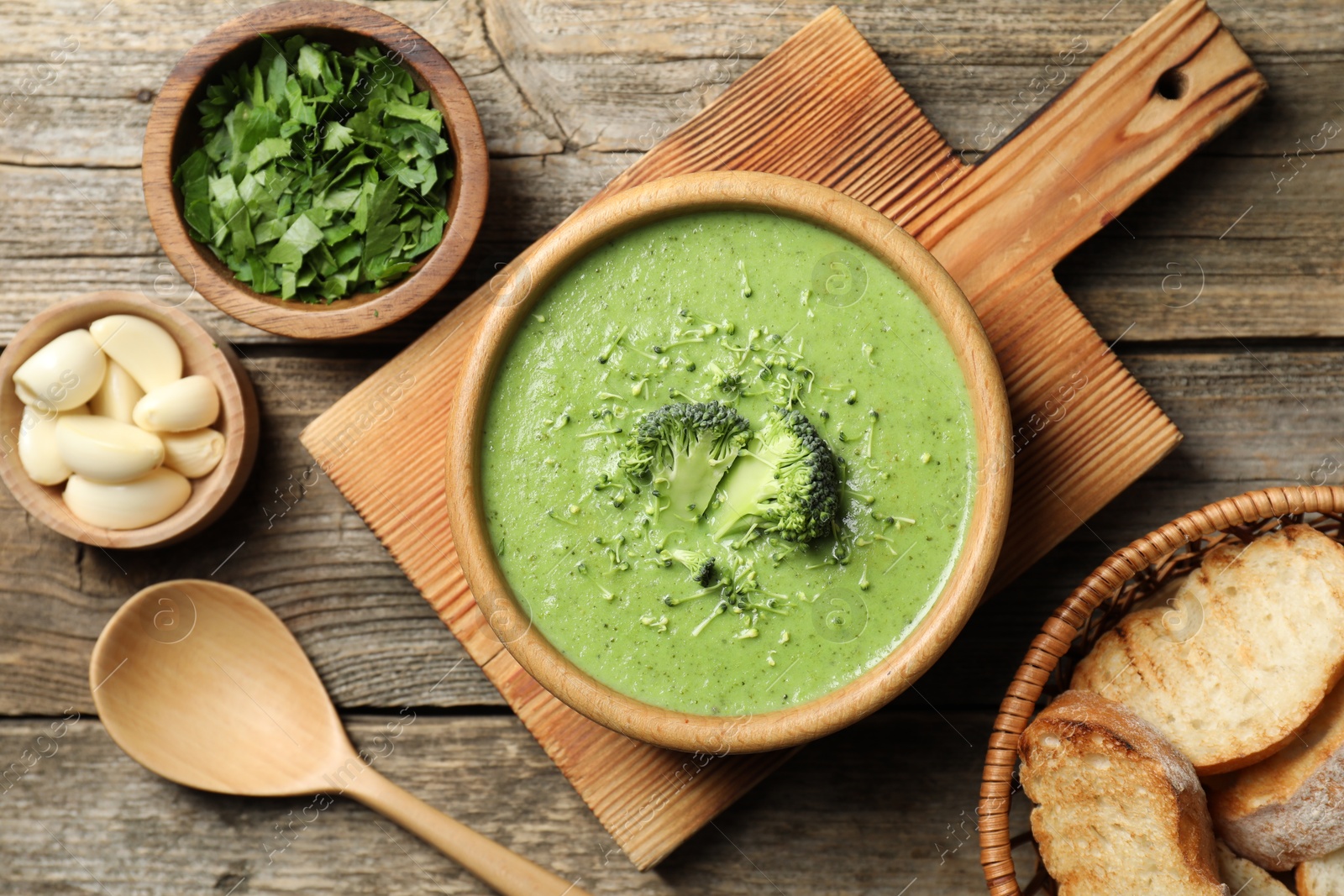 Photo of Delicious broccoli cream soup served on wooden table, flat lay