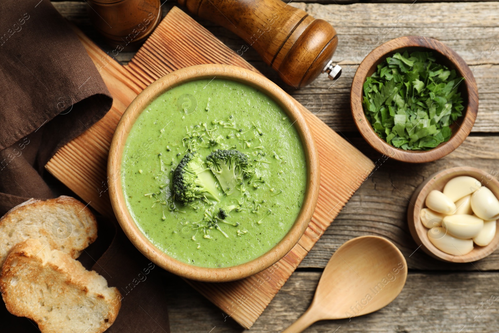 Photo of Delicious broccoli cream soup served on wooden table, flat lay