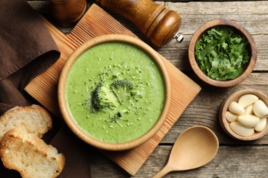 Photo of Delicious broccoli cream soup served on wooden table, flat lay