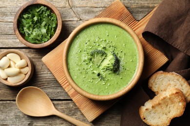 Photo of Delicious broccoli cream soup served on wooden table, flat lay