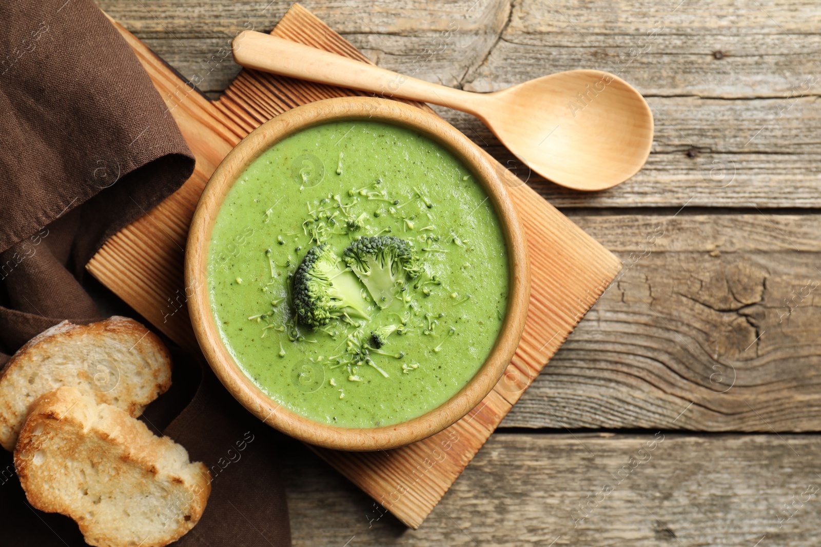 Photo of Delicious broccoli cream soup served on wooden table, flat lay