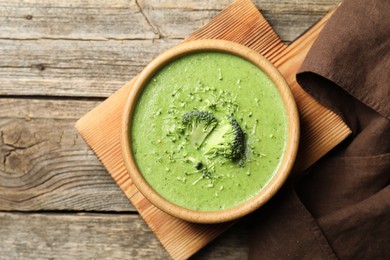 Photo of Delicious broccoli cream soup in bowl on wooden table, top view