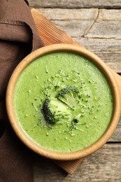 Photo of Delicious broccoli cream soup in bowl on wooden table, top view