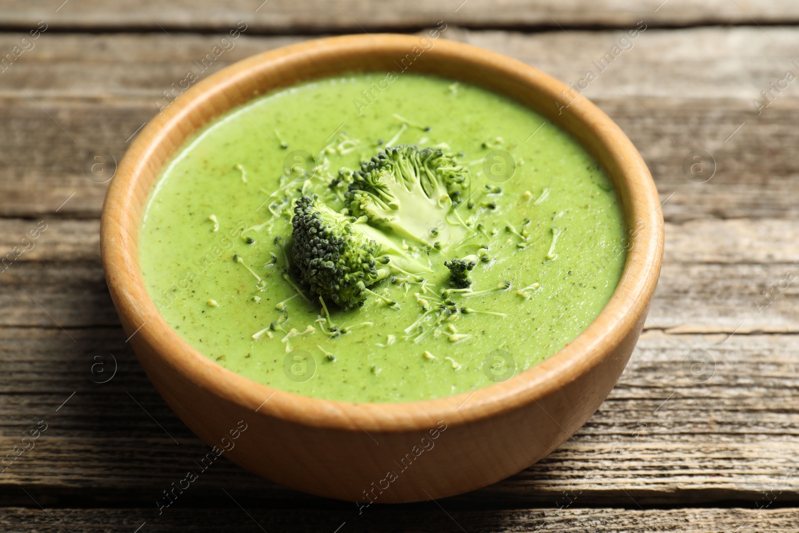 Photo of Delicious broccoli cream soup in bowl on wooden table, closeup