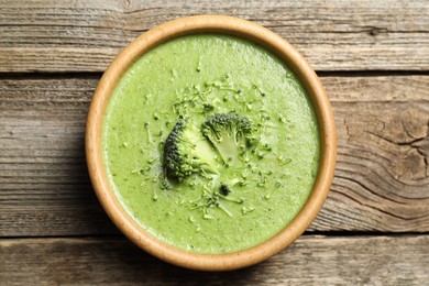 Photo of Delicious broccoli cream soup in bowl on wooden table, top view