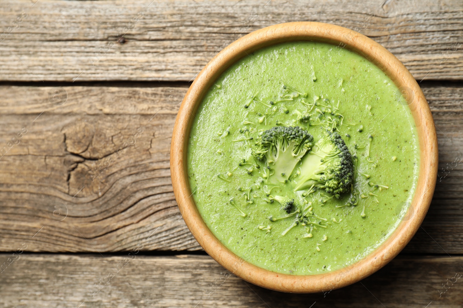 Photo of Delicious broccoli cream soup in bowl on wooden table, top view. Space for text