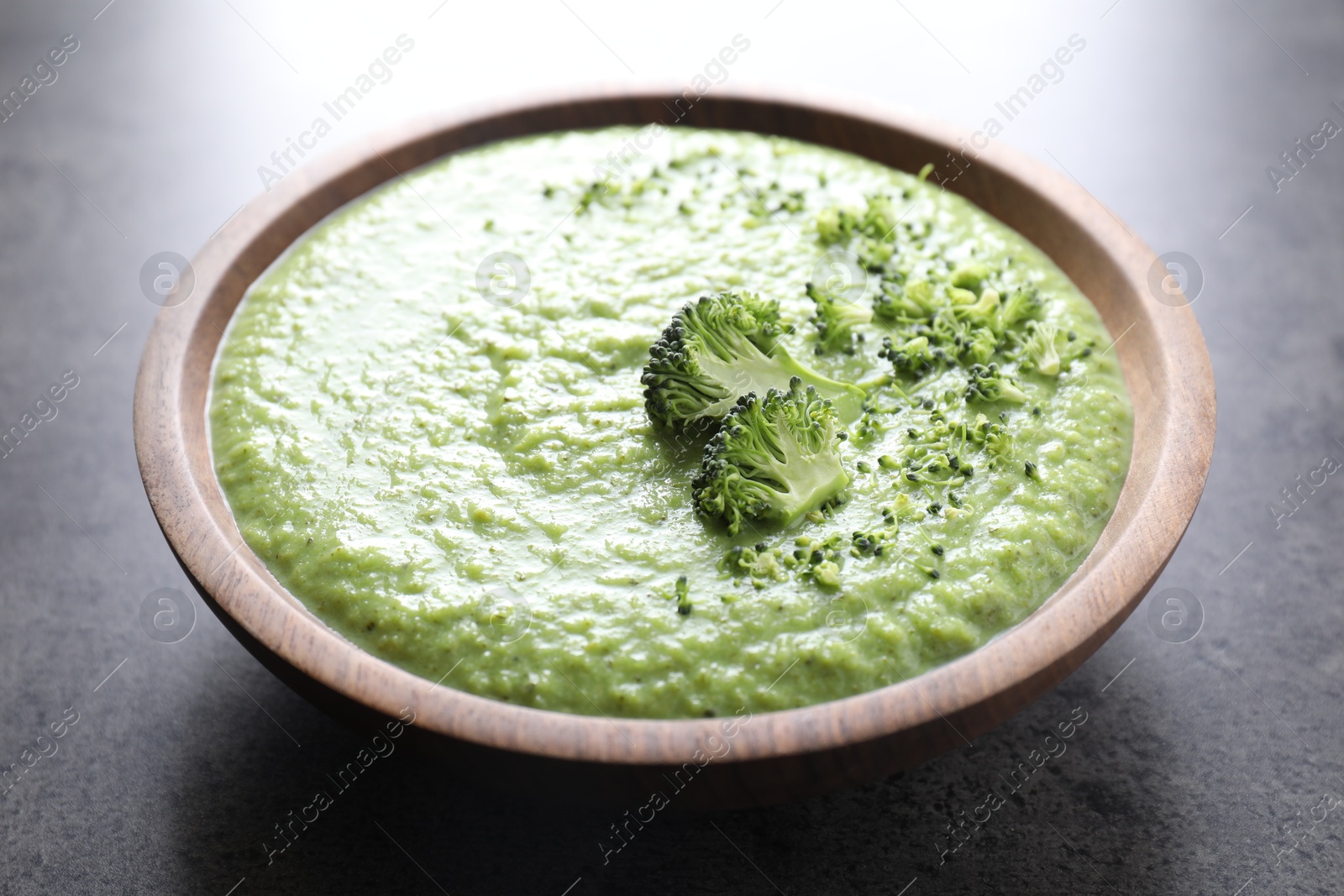 Photo of Delicious broccoli cream soup in bowl on grey table, closeup