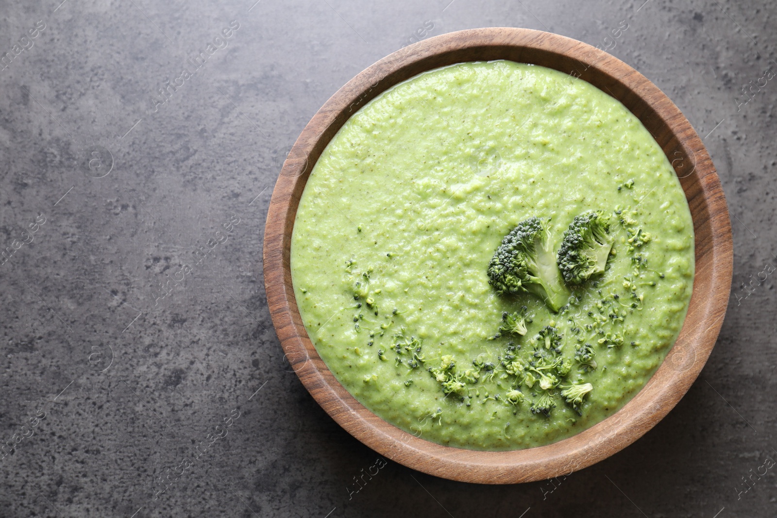 Photo of Delicious broccoli cream soup in bowl on grey table, top view. Space for text