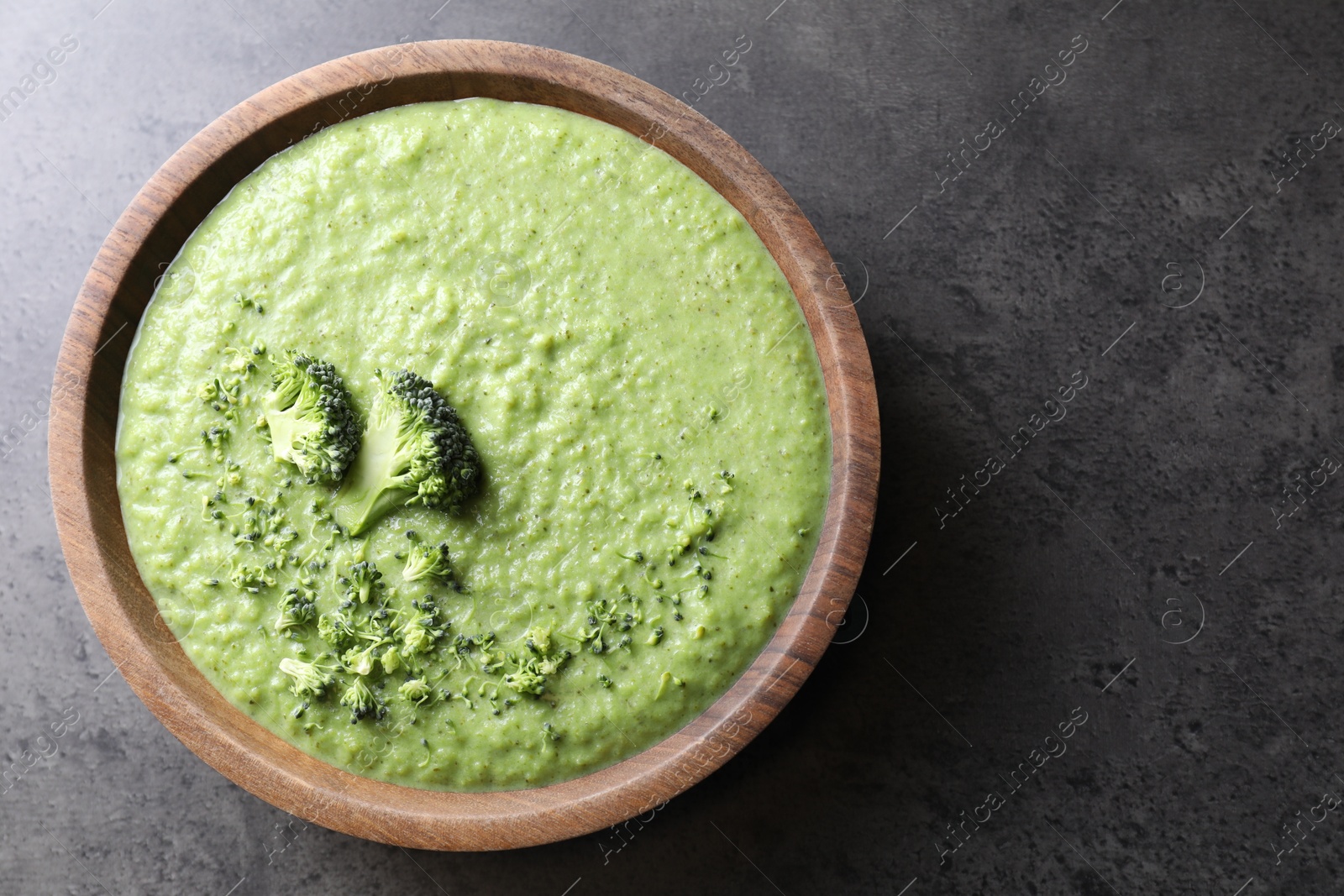 Photo of Delicious broccoli cream soup in bowl on grey table, top view. Space for text