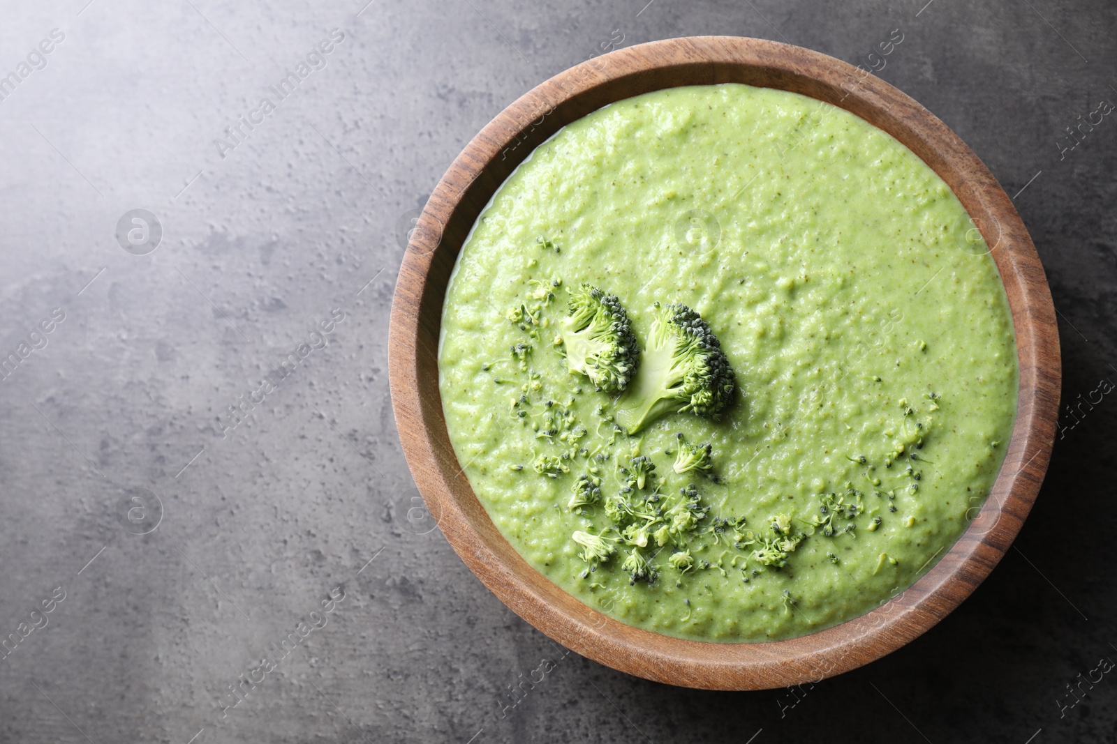 Photo of Delicious broccoli cream soup in bowl on grey table, top view. Space for text