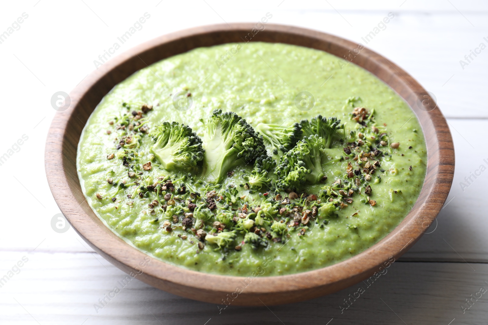 Photo of Delicious broccoli cream soup in bowl on white wooden table, closeup