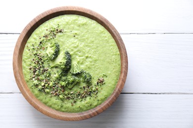 Photo of Delicious broccoli cream soup in bowl on white wooden table, top view. Space for text