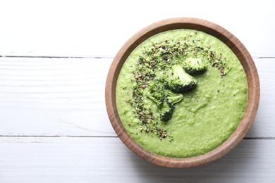 Photo of Delicious broccoli cream soup in bowl on white wooden table, top view. Space for text