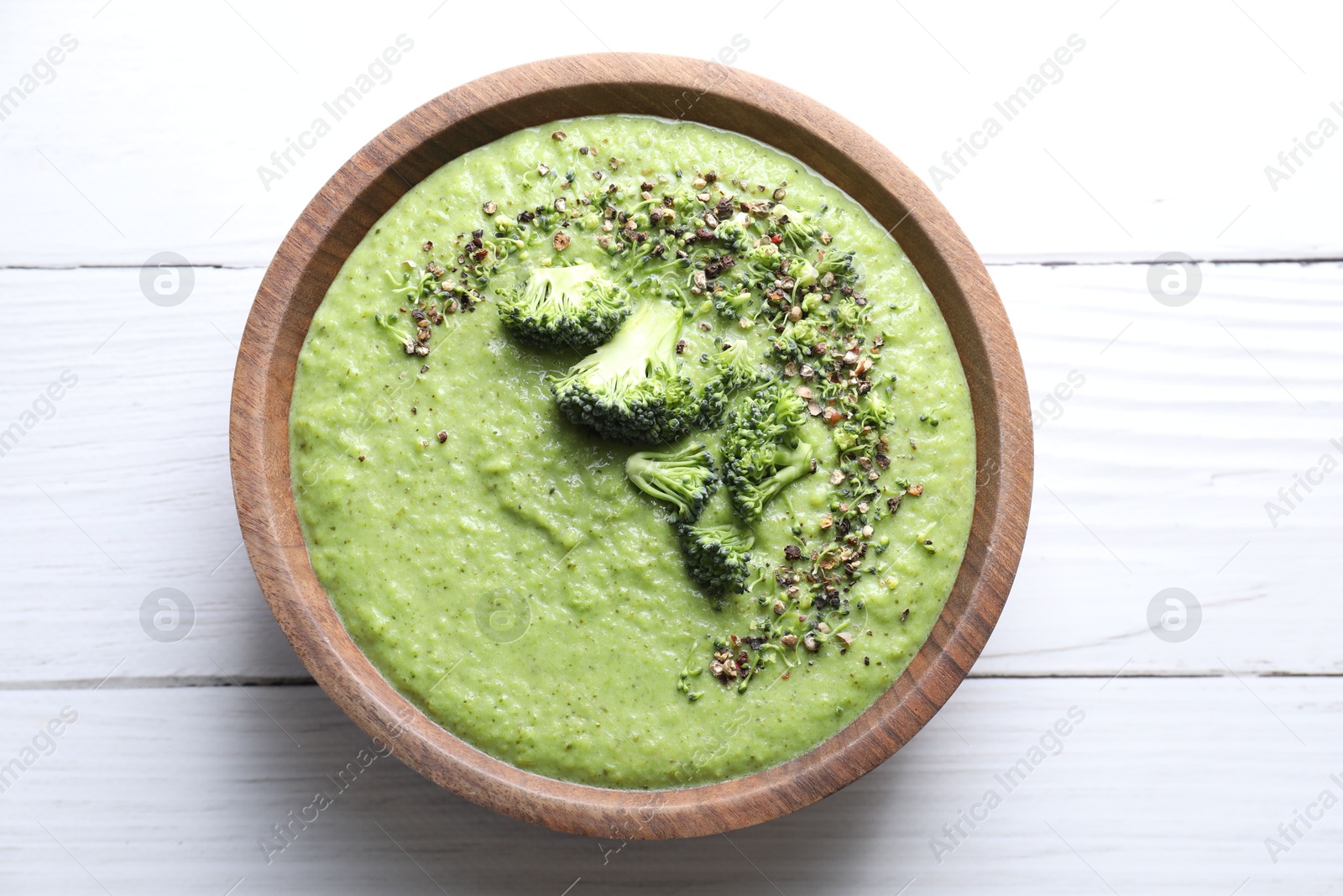 Photo of Delicious broccoli cream soup in bowl on white wooden table, top view