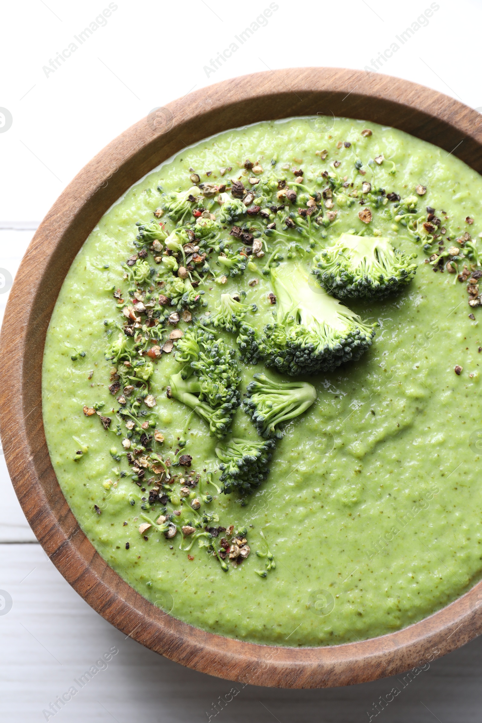 Photo of Delicious broccoli cream soup in bowl on white wooden table, top view