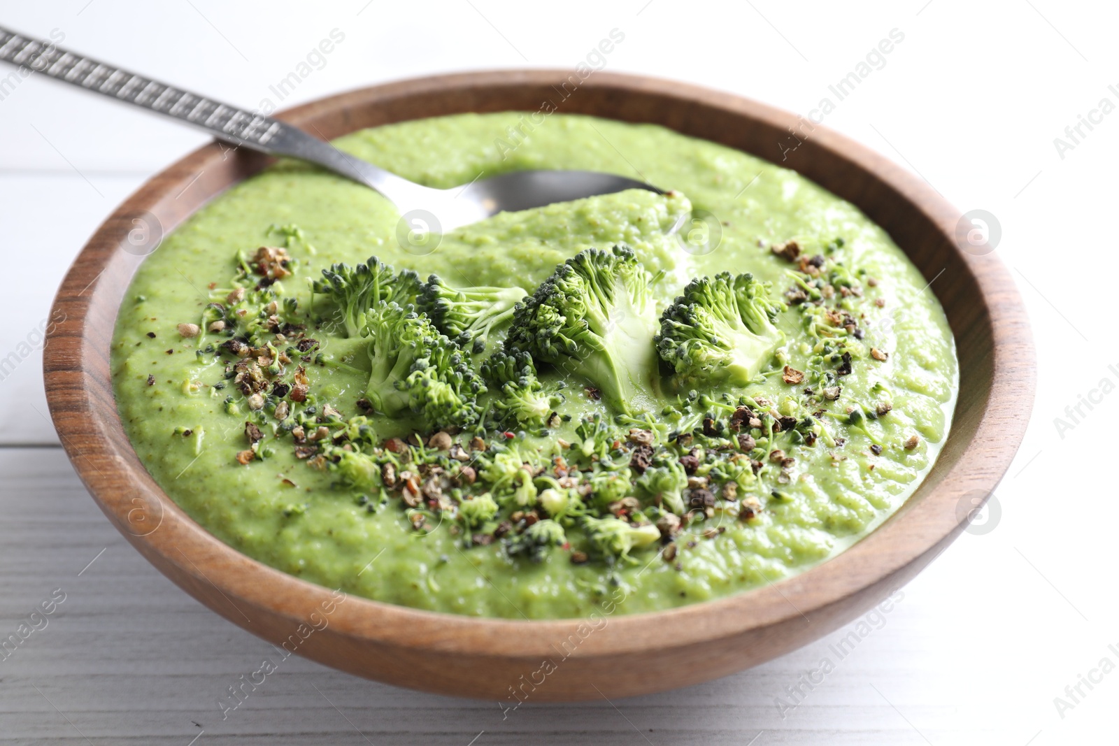 Photo of Delicious broccoli cream soup and spoon in bowl on white wooden table, closeup